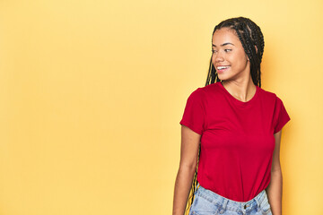 Young Indonesian woman on yellow studio backdrop looks aside smiling, cheerful and pleasant.