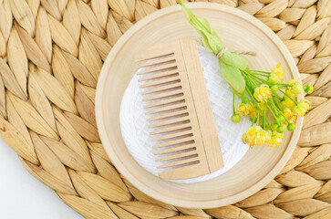 Small wooden plate with wooden hairbrush (comb) and linden (tilia, basswood, lime tree) flowers. Natural hair care, homemade spa and beauty treatment recipe.