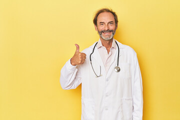 Doctor with stethoscope in yellow studio smiling and raising thumb up