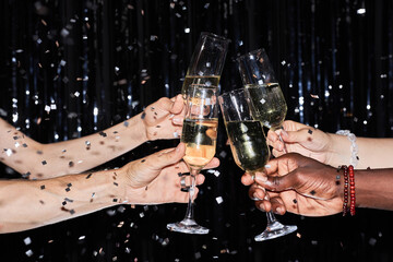 Closeup of multiethnic group of friends toasting with champagne glasses at party against glittering background with confetti