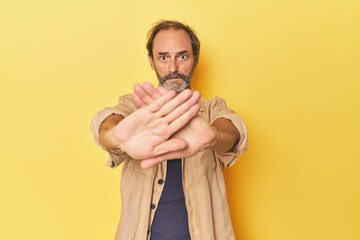 Caucasian middle-aged man in yellow studio doing a denial gesture