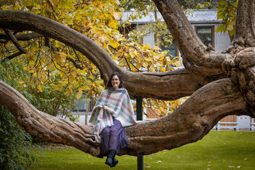 Caucasian woman in her 40s with black hair sitting in a tree branch looking at camera. Front picture.