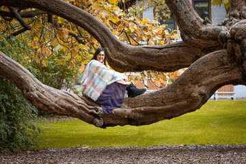 Caucasian woman in her 40s with black hair sitting in a tree branch looking at camera