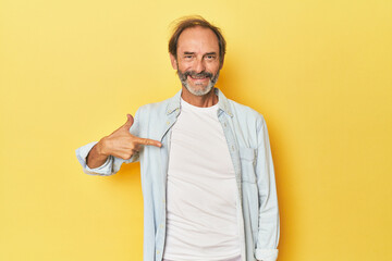 Caucasian middle-aged man in yellow studio person pointing by hand to a shirt copy space, proud and confident