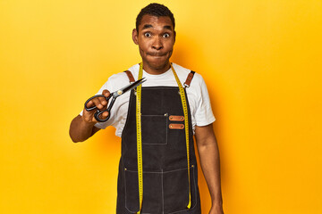 African American tailor with tools, yellow studio, confused, feels doubtful and unsure.