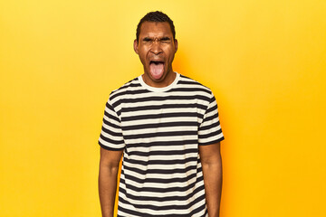 African American man in striped t-shirt, yellow studio, funny and friendly sticking out tongue.