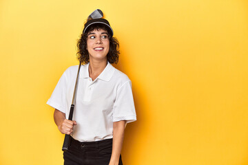 Athletic Caucasian woman with curly hair golfing in studio looks aside smiling, cheerful and...