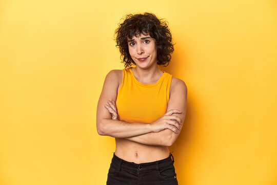 Curly-haired Caucasian woman in yellow top suspicious, uncertain, examining you.