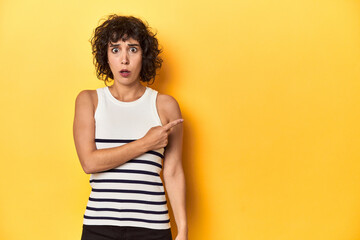 Caucasian curly-haired woman in white tank-top pointing to the side