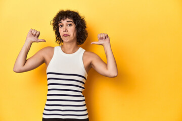 Caucasian curly-haired woman in white tank-top feels proud and self confident, example to follow.