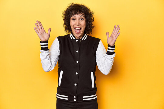 Curly-haired Caucasian woman in baseball jacket celebrating a victory or success, he is surprised and shocked.