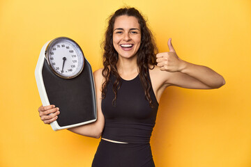 Young Caucasian woman with scale, weight management concept, yellow background. - obrazy, fototapety, plakaty