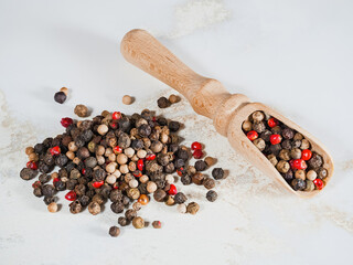 Mixture of red, white and black peppercorns in a wooden spice scoop and a handful of spices nearby