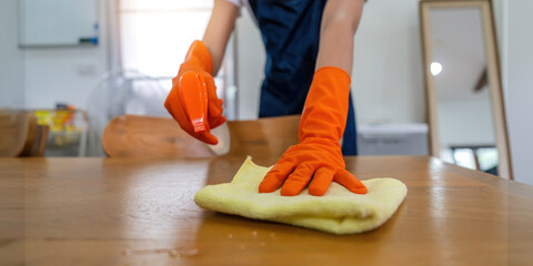 Asian woman wear rubber protective orange gloves sit clean guest reception desk with product and equipment cleaner at home