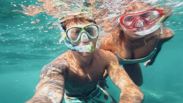 Beautiful and cute couple of millennials young people snorkeling and diving together looking underwater for fishes and coral having fun and enjoying. Summer time swimming in the sea blue ocean.
