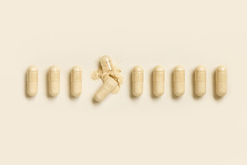 Medical capsules in a line with one opened to show beige powder top view. Dietary supplements
