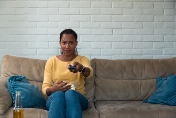 Young scared woman sitting alone at home on the sofa watching scary horror movie on the television....