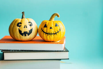 Beautiful jack o lantern pumpkins sitting on a stack of books on a blue background.Creative halloween concept backdrop.Autumn reading concept. Books for fall to read. Kids halloween pumpkin craft.
