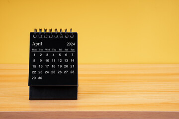 The April 2024, Monthly desk calendar for 2024 year on wooden table with yellow background.