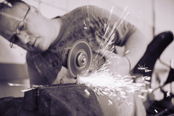 A master in glasses grinds a part clamped in a vice with a grinder