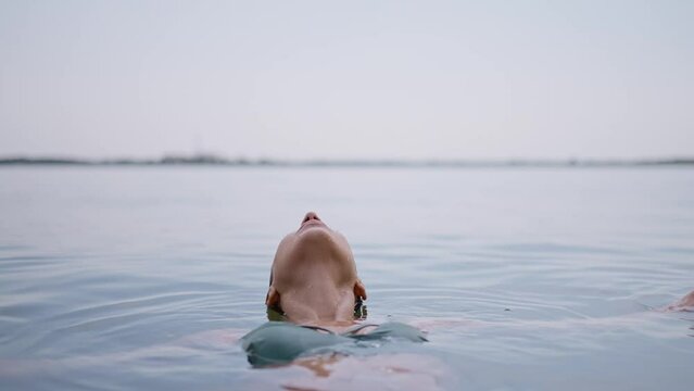 young adult woman relaxes lying on water surface in lake, eyes closed contentedly as she enjoys a dip in water. woman standing up from water. young model plunged into sea. Tropical vacation enjoyment