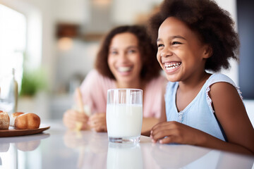 Little african-american girl and mother happily drinking milk on kitchen - obrazy, fototapety, plakaty