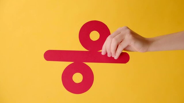 Vertical video of female hand holding big paper red percent mark, presenting big discounts, isolated over yellow color background wall in studio with copy space for promotion content or desing