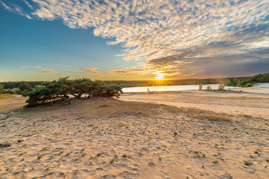 A dramatic and colourful sunset over the Lommelse Sahara, a National Park with sand dunes in Belgium with beautiful reflections in the lake of the clouds and natural colours.