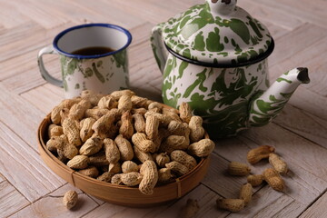 peanuts in a woven bamboo container on wooden table. Arachis hypogaea. a teapot and a cup of tea. tea time. 