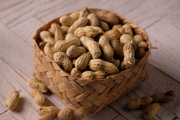 peanuts in a woven bamboo container on wooden table. Arachis hypogaea