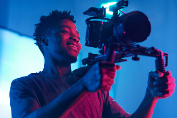 Young African American cameraman shooting with professional camera in studio