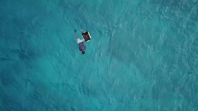 Drone post view of asian man floating in the Indian ocean and searching seashells.Maldives