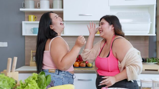 Happy plus size asian women dancing in the kitchen at home. having fun, Body positivity, Body acceptance party concept.