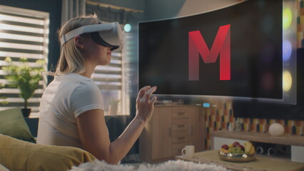 Woman in VR headset chooses movie or TV show to watch at home. 3D futuristic hologram shows interface of streaming service application and widgets in user menu. VFX animation. Concept of lifestyle.
