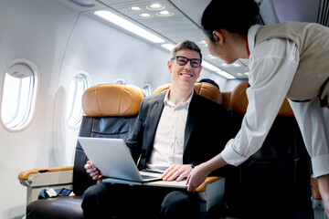 Busy businessman working on laptop computer inside airplane, air hostess warning male passenger...