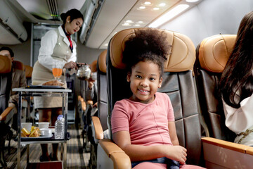Happy African girl child, kid passenger sitting in comfortable seat inside airplane during female...