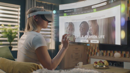 Woman in VR headset chooses clothes in online store chilling at home. 3D futuristic hologram shows widgets in user menu and clothing store website interface. VFX animation. Concept of online shopping.