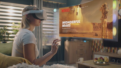 Woman in VR headset chooses movie or TV show to watch at home. 3D futuristic hologram shows interface of streaming service application and widgets in user menu. VFX animation. Concept of lifestyle.