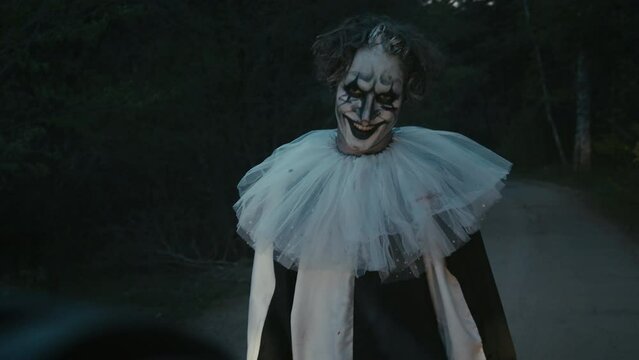 Medium shot of creepy clown running after car on road at night