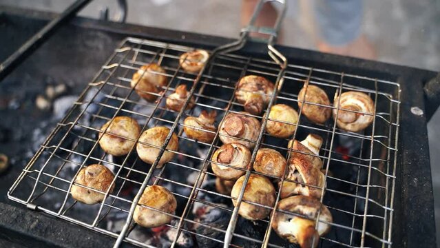 Close-up of grilled mushrooms champions in bbq grill net with hot coal underneath. Grilling cooking food outdoors in nature, simple food on weekend