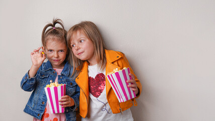 two happy little sisters eating sweet popcorn with dragee candies on gray background