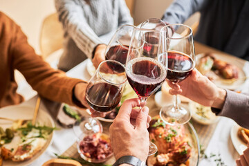 Close up of people toasting with red wine glasses at festive dinner table, copy space