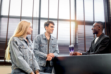 Cute couple lover sitting by table in bar having cocktail drink and friendly African bartender standing behind counter bar making drinks to serve customers, happy people enjoying at night club lounge.