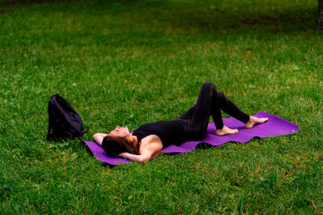 Active beautiful yogi woman resting in the city park after training lying on a fitness mat looking at the sky