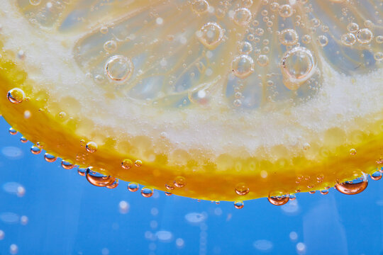 Macro shot of curved edge of see through lemon slice on blue background with fizzy bubbles
