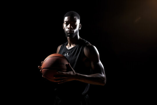 Basketball player concentrating on game. Young african american man holding ball with both hands on black background.