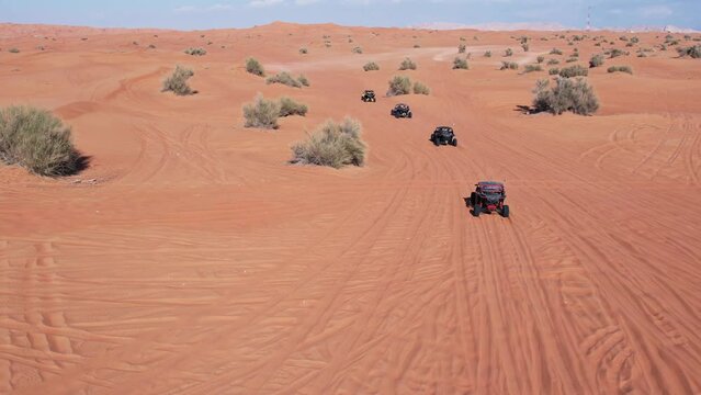 A drone flies over a caravan of buggies driving through the desert sand