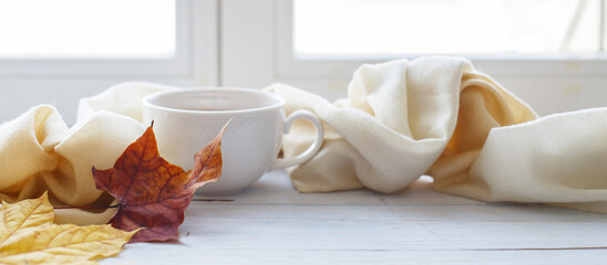 autumn leaves with a cup of tea or coffee next to a scarf on a wooden background banner