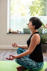 Brunette middle aged woman doing yoga meditation on exercise mat at home, mental health. Peaceful woman meditate, mental balance, time for herself, stress relief, mediation, mind fullness concept