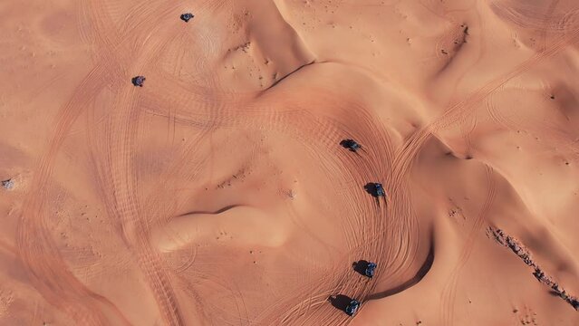 A drone flies over a caravan of buggies driving through the desert sand